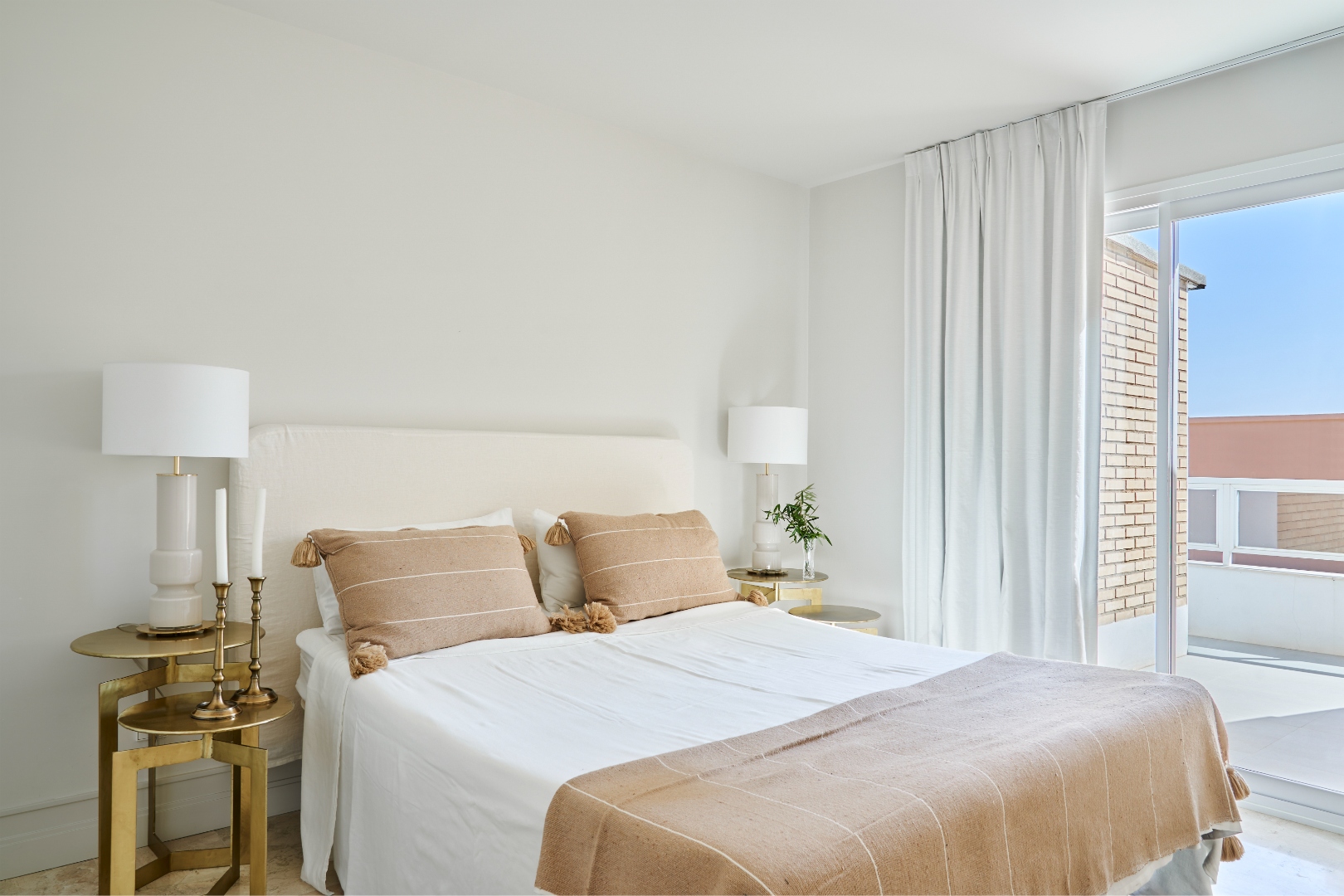 Second bedroom detail — brass side table, tasselled cushions, warm linen throw