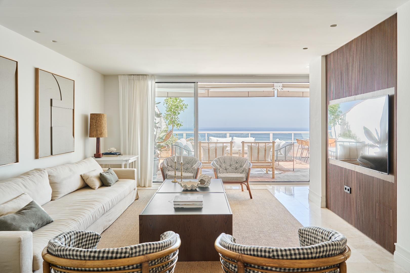 Terraza Del Sol living room — sofa, gingham chairs, walnut TV panel, terrace open to sea