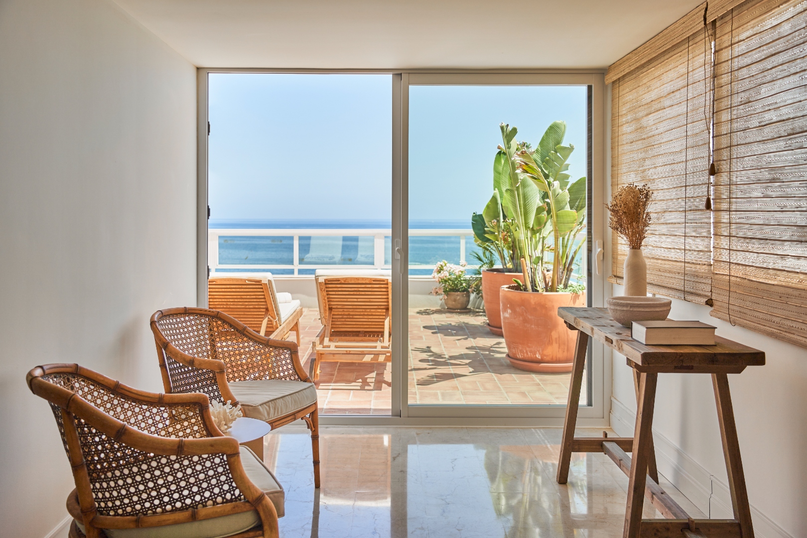 Sitting area — rattan chairs, sea view through terrace door, bamboo blinds