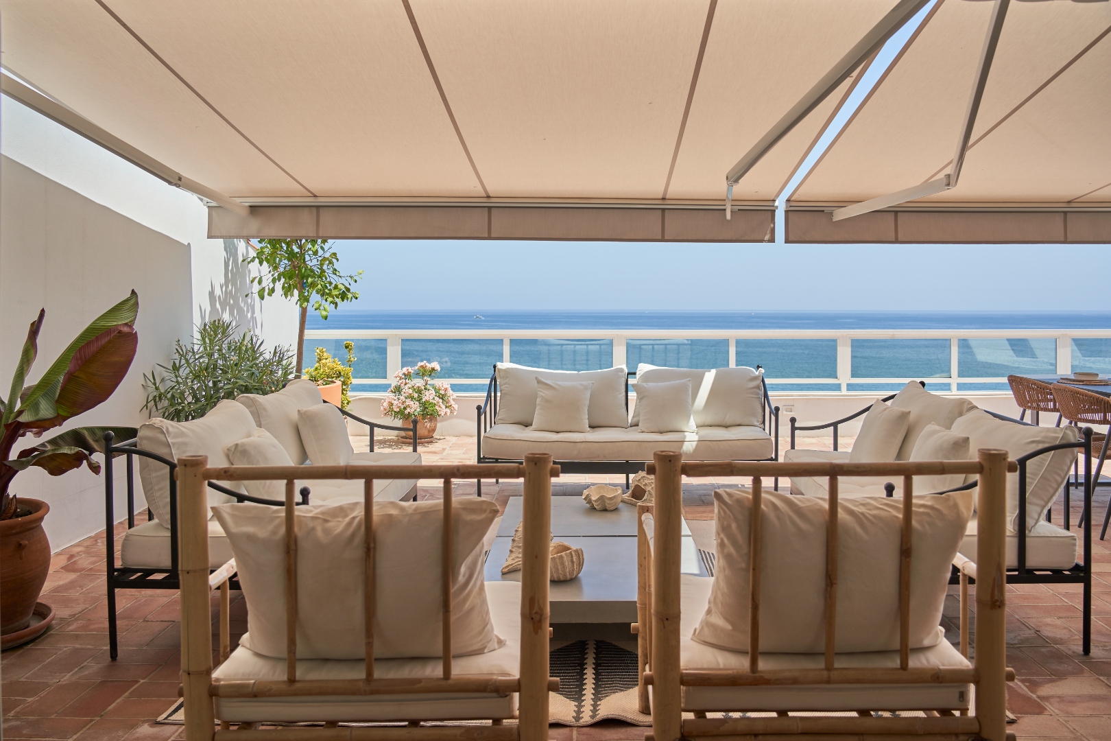 Terraza Del Sol terrace lounge — white sofas and bamboo chairs facing the sea under awning