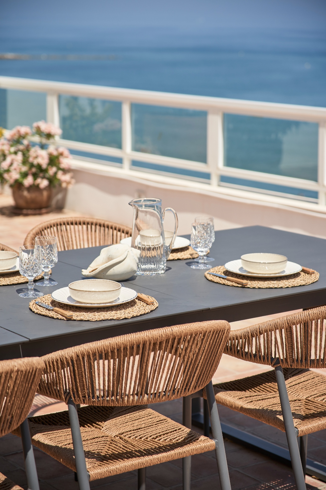 Terrace dining close-up — crystal glasses, woven placemats, sea behind